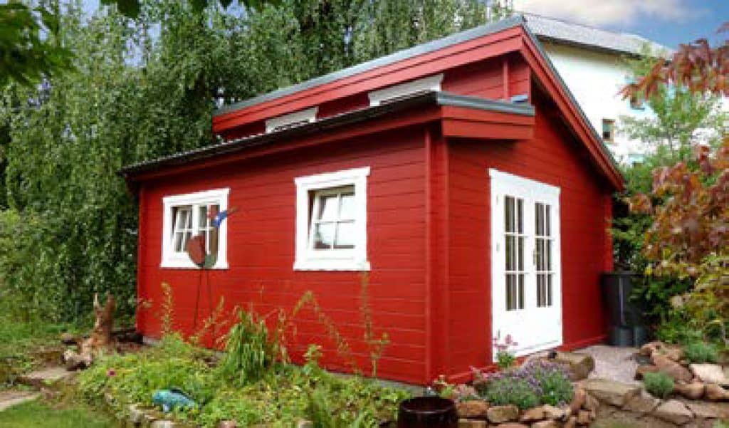 Ein rotes Blockhaus mit weißen Sprossenfesnter und weißer doppelflügeliger Sprossentür